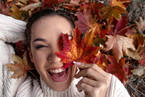 Portrait of a beautiful woman hold the fall leaves and resting in the park. The happy girl wearing knitted sweate