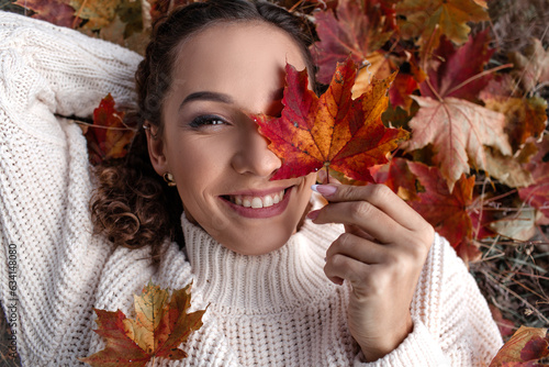 Portrait of a beautiful woman hold the fall leaves and resting in the park. The happy girl wearing knitted sweate