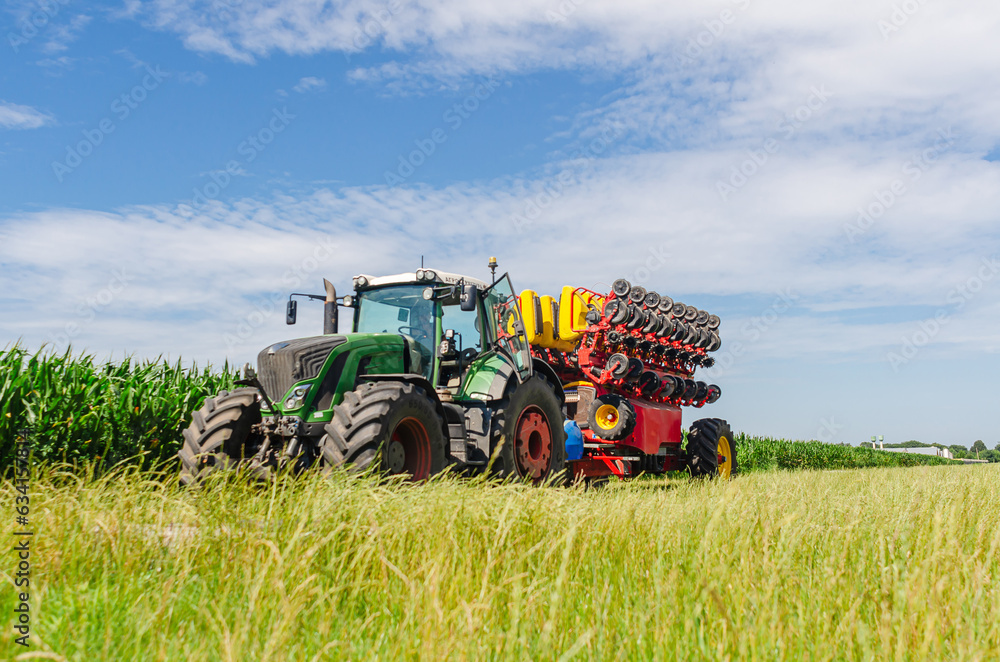 Seeder tractor in green corn field. Low angle view. Bright agricultural landscape with machinery. Seeder tractor in green corn field. Low angle view. Bright agricultural landscape with machinery.
