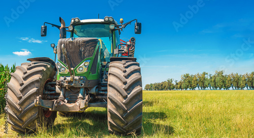 Fototapeta Naklejka Na Ścianę i Meble -  Large tractor on a summer field. Front view. Trees in the background. Agricultural landscape