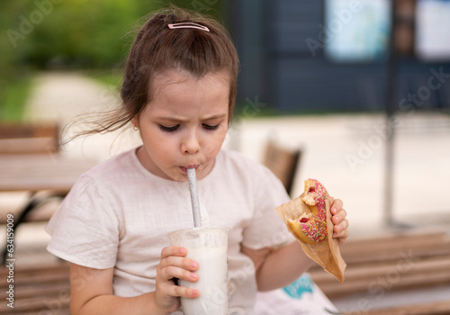 A six-year-old girl drinks a milkshake and eats a kidney. Sweets in children s lives  street food.