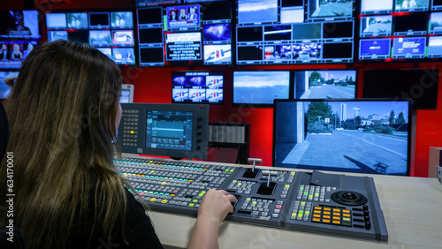 The director in the TV control room at the video mixer. Video switcher operator using the video mixer. Numerous screens in the TV control room. TV employee broadcasting live.
