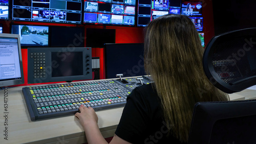 The director in the TV control room at the video mixer. Video switcher operator using the video mixer. Numerous screens in the TV control room. TV employee broadcasting live.
