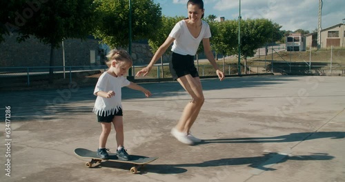 Young mother teach her daughter to ride on skateboard at sport field on summer