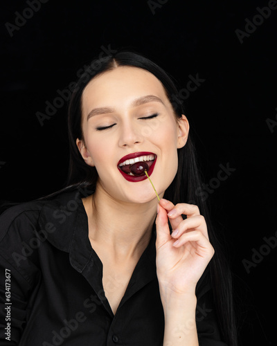 Young woman eats cherries. Sexy red lips with ripe organic cherry  isolated on black background.
