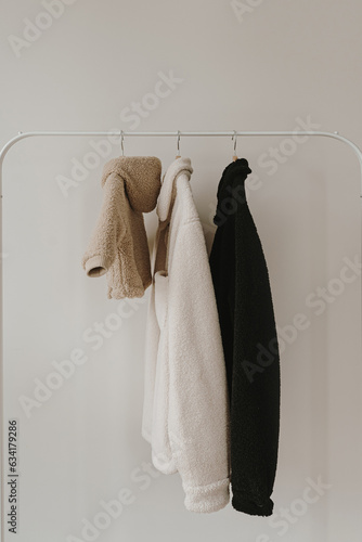 Warm autumn seasonal baby and adult clothes on hanger over white wall. Woolen neutral beige, white and black jackets. Minimalist fashion clothes wardrobe