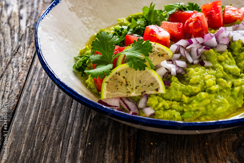 Guacamole with tomato, red onion and parsley on wooden table Guacamole with tomato, red onion and parsley on wooden table