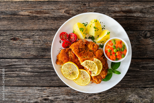 Photography Crispy breaded seared chicken cutlet with boiled potatoes and vegetables on wood