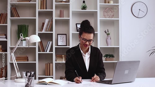 Latin American girl works in the office. He signs the agreement and smiles at the camera. Secretary. E commerce. Freelancer. Office, Formal wear, laptop.