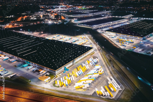 Many warehouses in an industrial area, aerial view of brightly lit logistics warehouses at night, trading business