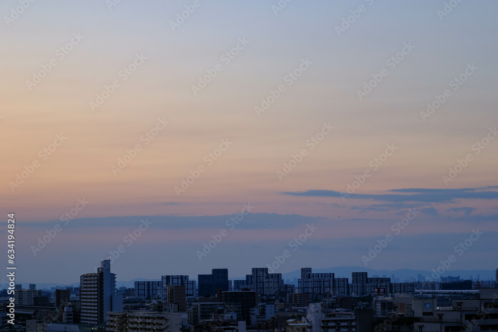 都市の夜明け。東の空が明るくなり雲がまだ昇る前の太陽に照らせら美しいグラデーションを見せる。神戸市内から大阪方面を臨む。