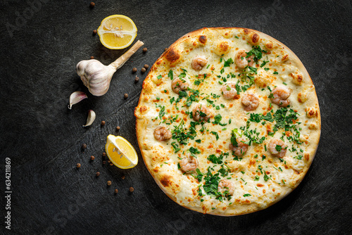 Pizza with shrimp and parsley on a black background with lemon, garlic and peppers, top view