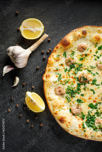 Pizza with shrimp and parsley on a black background with lemon, garlic and peppers, top view
