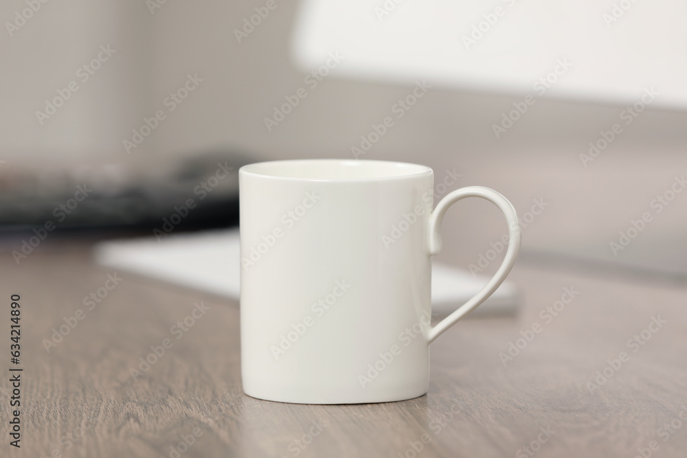 White ceramic mug and computer on wooden table at workplace