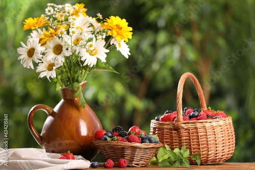 Different fresh ripe berries and beautiful flowers on table outdoors