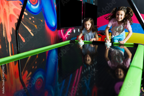 Little girls having fun in the arcade playing air hockey photo