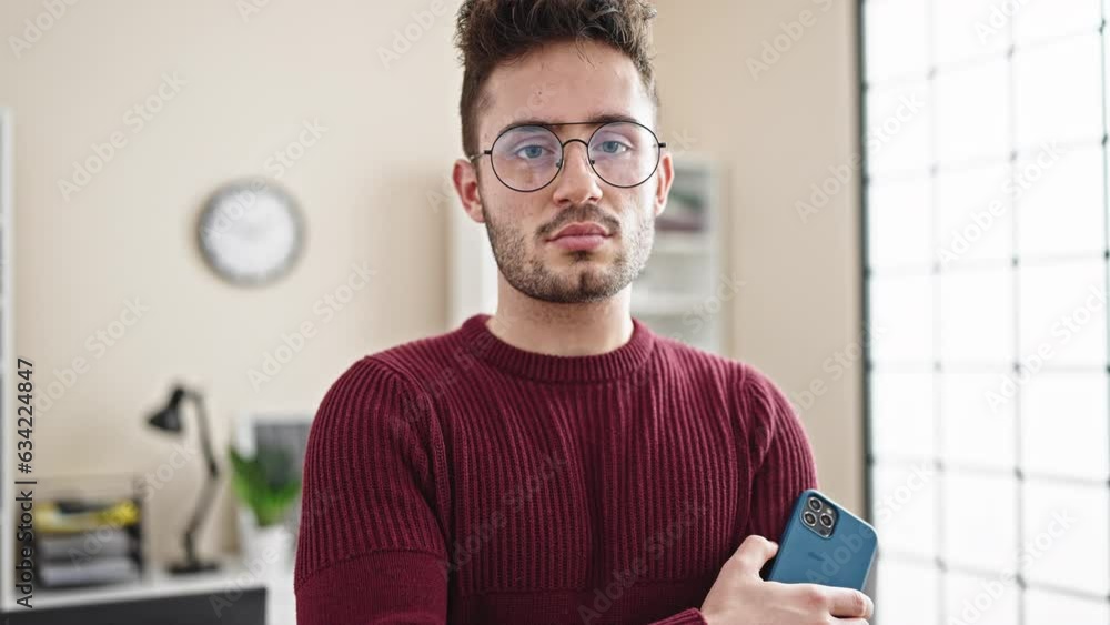 Young hispanic man business worker standing with arms crossed gesture holding smartphone at office Young hispanic man business worker standing with arms crossed gesture holding smartphone at office