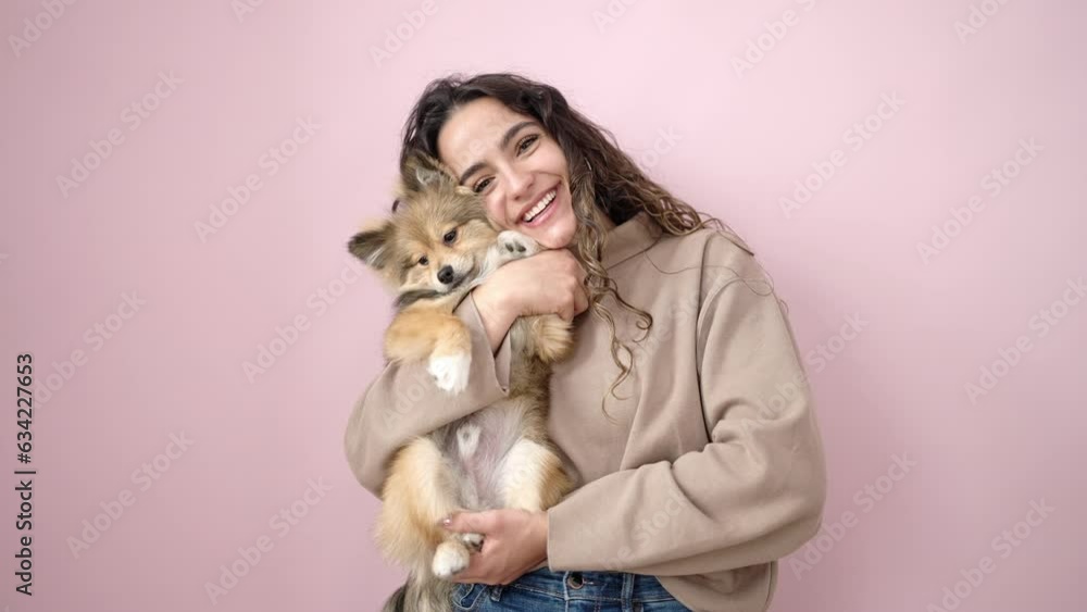 Young hispanic woman with dog smiling confident standing over isolated pink background Young hispanic woman with dog smiling confident standing over isolated pink background