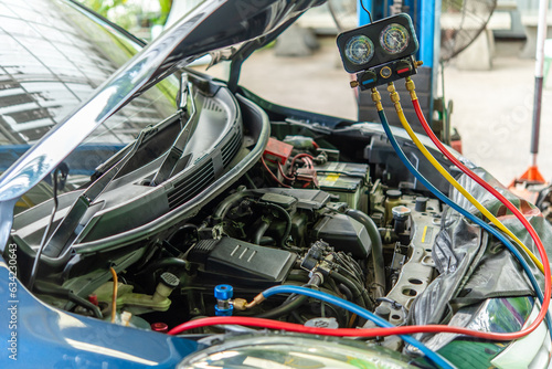 Car mechanic or serviceman refilling air condition and checking a air compressor for fix and repair problem at car garage or repair shop © pongmoji