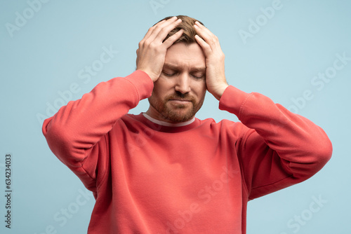Portrait of sad man having life troubles holding head with suffering face on studio blue background. Frustrated, confused male with headache, life problems, midlife crisis. Stress, panic, desperation. photo