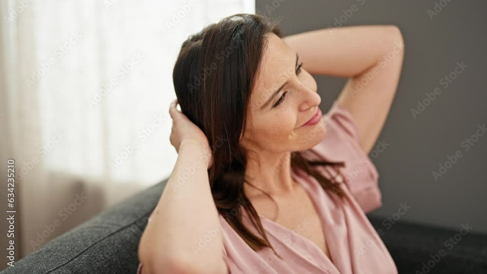 Young beautiful hispanic woman smiling confident sitting on sofa combing hair with hand at home Young beautiful hispanic woman smiling confident sitting on sofa combing hair with hand at home