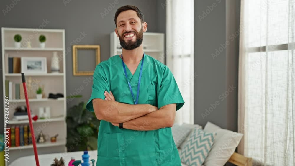 Young hispanic man professional cleaner standing with arms crossed gesture smiling at bedroom Young hispanic man professional cleaner standing with arms crossed gesture smiling at bedroom