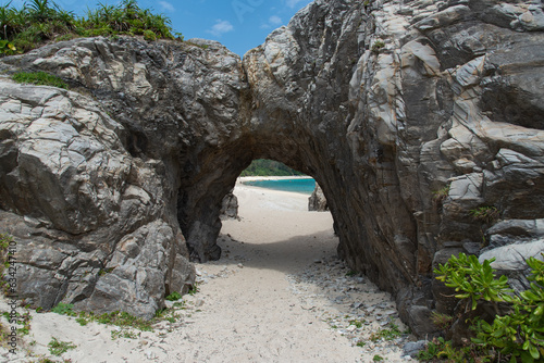 岩のトンネルの向こうに広がる白い砂浜とエメラルドグリーンの海
