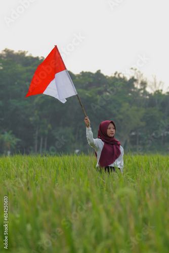 Asian woman in white shirt waving Indonesian flag excitedly in rice field.
