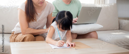 Φωτογραφία Happy family with mother teaching homework with daughter and father working with laptop on sofa in living room at home, mom explaining schoolwork with kid together, lifestyles and education