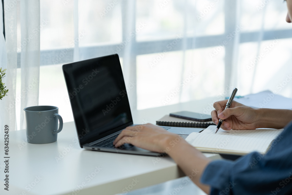 Fototapeta premium Young businessman, asian office worker sitting working on laptop computer in office data research concept note taking online learning