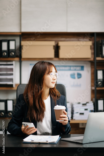 Confident Asian woman with a smile standing holding notepad and tablet at the modern office.