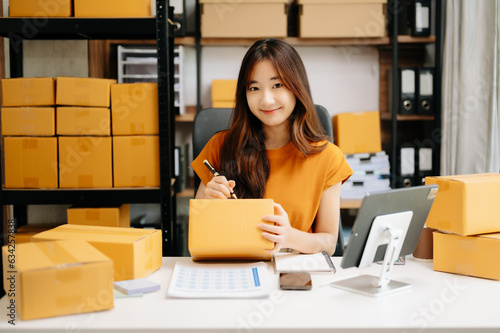Startup small business SME, Entrepreneur owner woman using smartphone or tablet taking receive and checking online purchase shopping order to preparing pack product box. . © Nuttapong punna