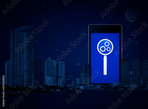 Seo flat icon on modern smart mobile phone screen over office city tower, river and fantasy night sky, Search engine optimization concept