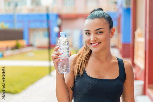 Young pretty woman with a bottle of water at outdoors smiling a lot