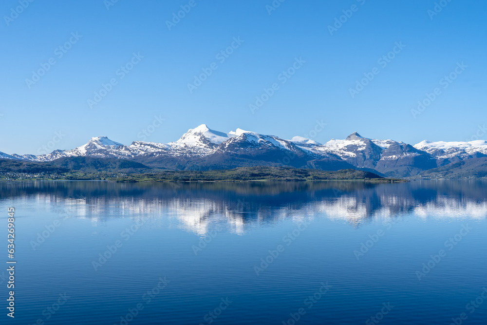 Snow covered fjords in Norway reflected in calm ocean