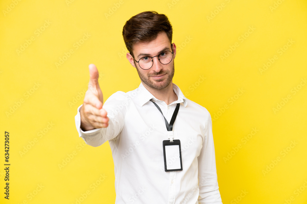 Young caucasian with ID card isolated on yellow background shaking hands for closing a good deal Young caucasian with ID card isolated on yellow background shaking hands for closing a good deal