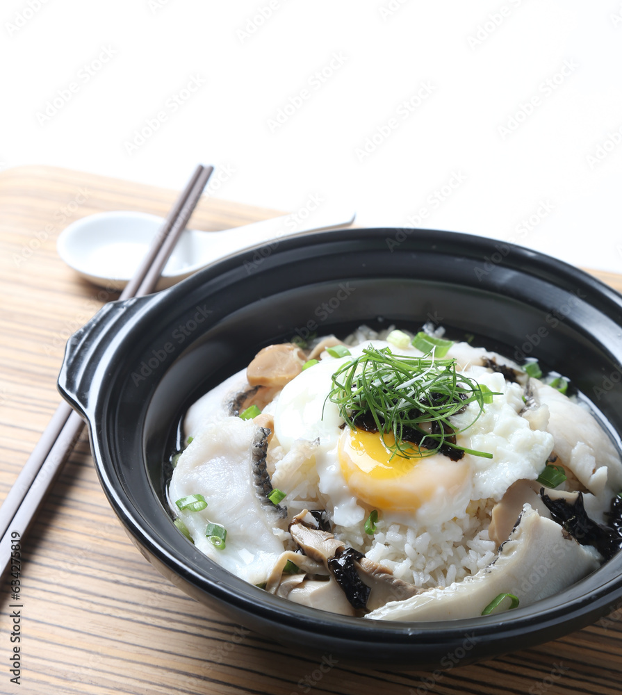 Hong Kong congee porridge rice with seafood fish, prawn, squid, mushroom, egg and vegetables in black hot clay pot on wood tray white background asian chef halal food restaurant banquet cafe menu