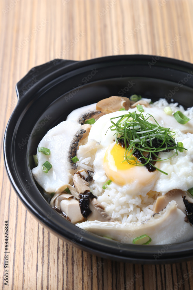 Hong Kong congee porridge rice with seafood fish, prawn, squid, mushroom, egg and vegetables in black hot clay pot on wood tray white background asian chef halal food restaurant banquet cafe menu