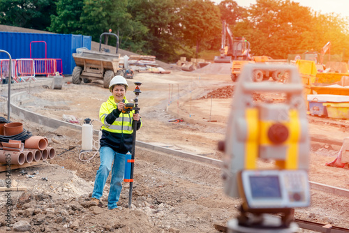 Happy Female site engineer surveyor working with theodolite total station EDM equipment on a building construction site outdoors