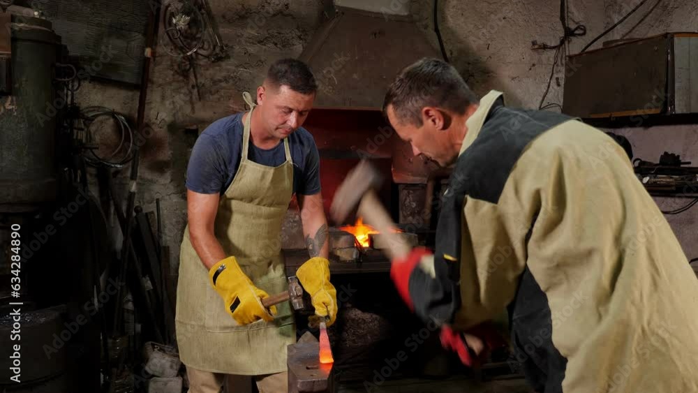 Strong brutal blacksmiths manually molten metal on an anvil in