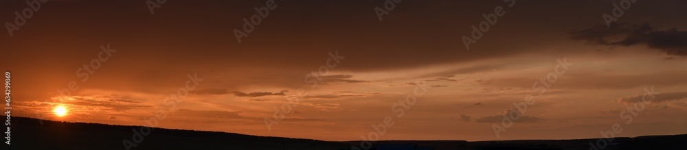 Panorama of a sunset evening with pink clouds and the sun. Beautiful evening clouds.