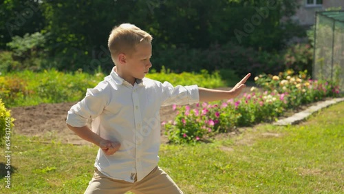 Caucasian boy practicing karate in casual clothes in park. Young kid training martial arts outdoors. Young sportsman. 4K, UHD