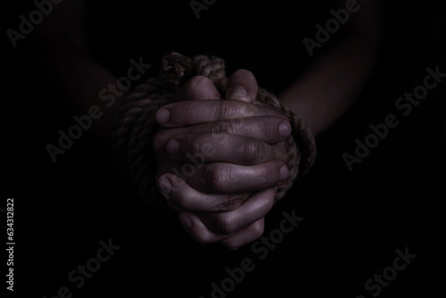 woman's hands tied with rope on black background, concept of domestic violence of the victim