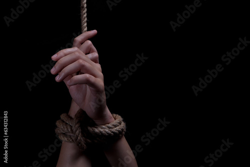 woman's hands tied with rope on black background, concept of domestic violence of the victim. copy space for text