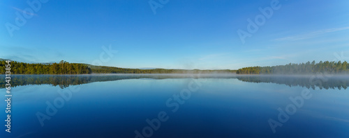The mirror-like tranquil lake surface reflects the reflection of woods and mountains in Sweden.