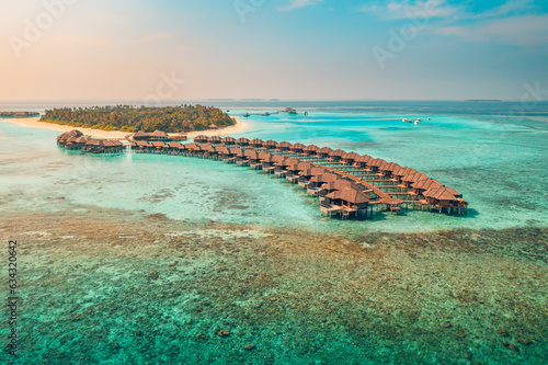 Sunset on Maldives island, luxury water villas resort and wooden pier. Beautiful aerial sky clouds and beach background. Summer coast vacation travel. Paradise sunrise landscape. Pristine sea bay