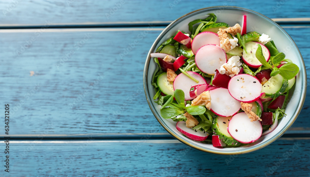 Tasty salad with radish in bowl on blue wooden table