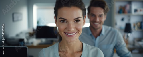 A young woman smiles brightly in her cozy office, surrounded by a computer, wall, and stylish clothing, her eyebrows slightly raised in joy photo