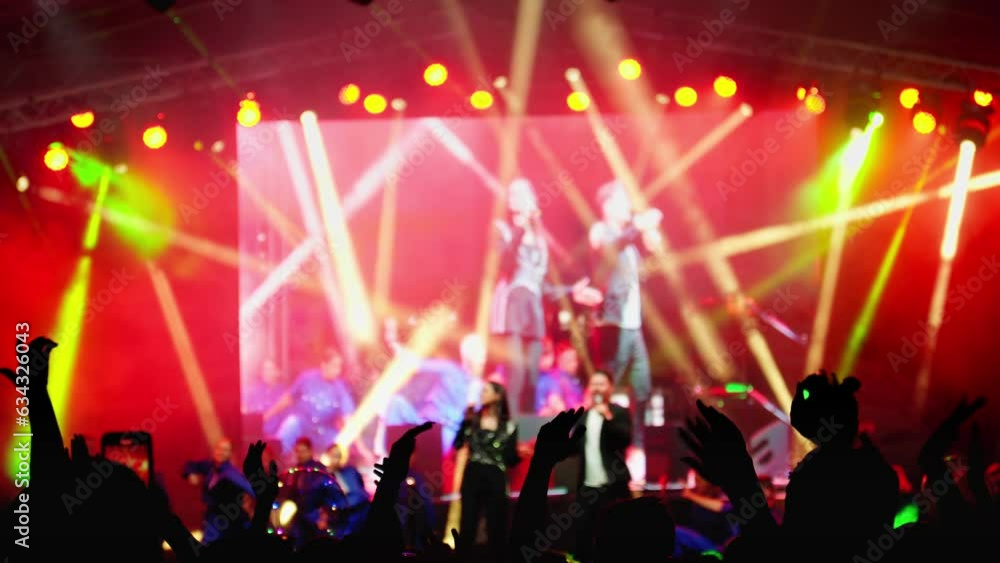 Big crowd at concert cheering clapping hands at night rock concert. Silhouettes of hand in concert. Crowd is partying. Bright colorful stage lighting. 4K, UHD Big crowd at concert cheering clapping hands at night rock concert. Silhouettes of hand in concert. Crowd is partying. Bright colorful stage lighting. 4K, UHD