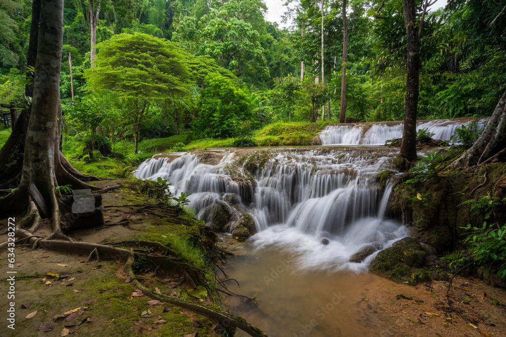 waterfall stream on nature clear motion water and green trees jungle in natural forest environment or rainforest at Kroeng Krawia waterfall in Thailand on rainy season cloudy for landscape background
